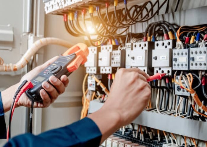 Electrician engineer uses a multimeter to test the electrical installation and power line current in an electrical system control cabinet.