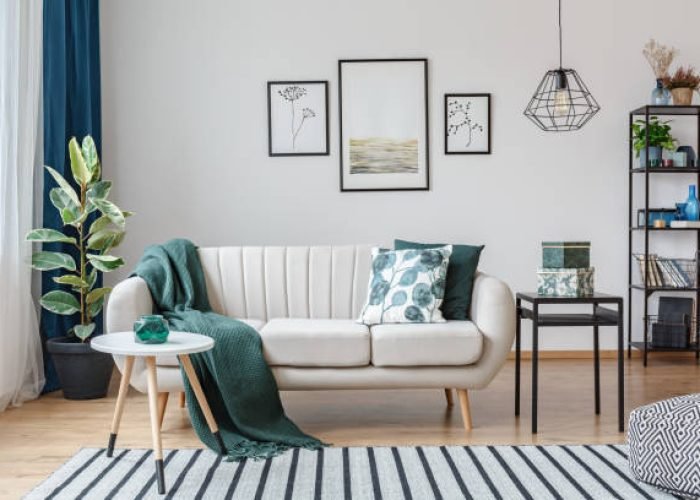 Black table next to sofa with green blanket in cozy apartment interior with gallery of posters